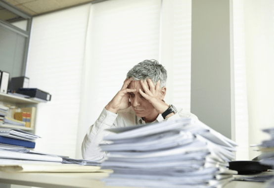 デスクで書類を見て困った様子の人